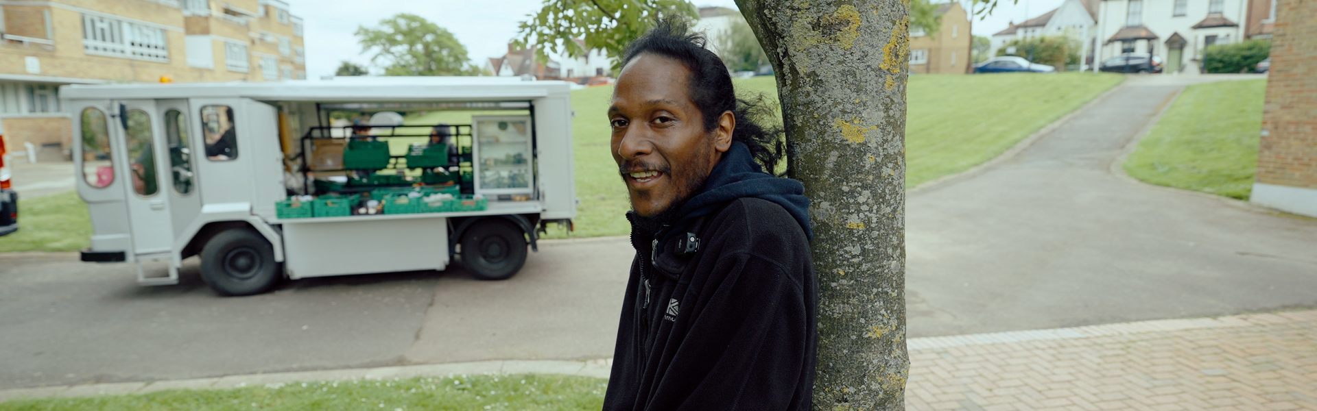 Man on crutches leans on tree in front of food hub van